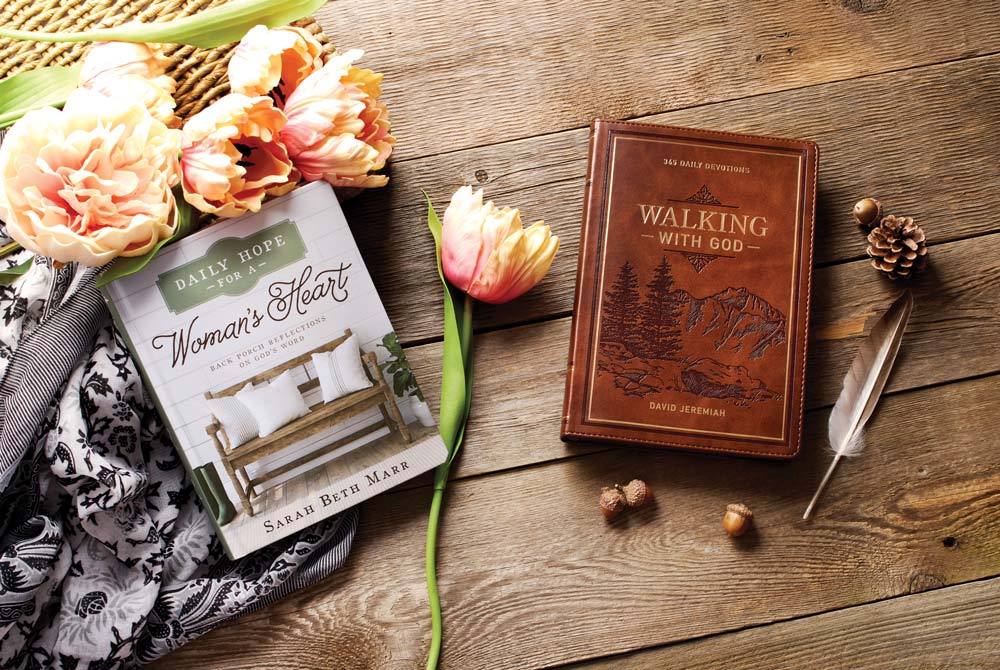 Two books, white one titled Daily Hope for a Woman's Heart and brown one Walking with God, lying on wood surface with flowers